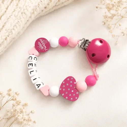 Attache tétine cœur pailleté rose personnalisée avec le prénom Célia dans un décor doux Kids and Crea