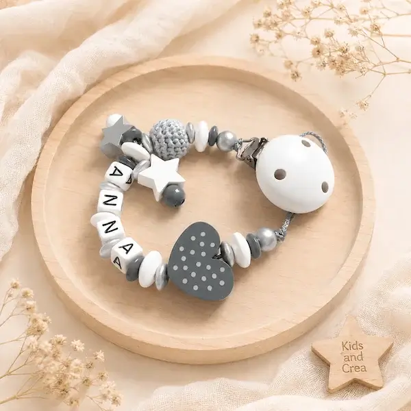Accroche tétine mixte en bois FSC avec prénom Anna, perle crochet grise, cœur gris, étoiles blanches et perles argentées.